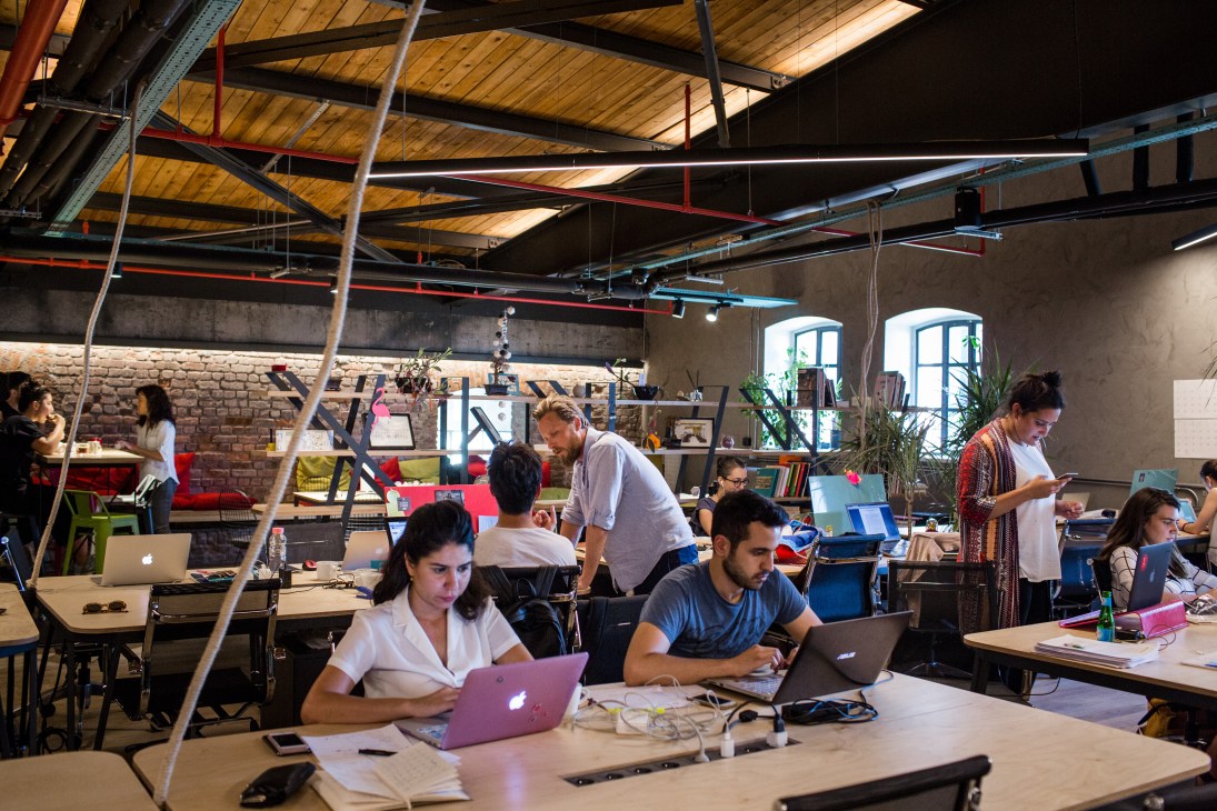 Freelancers work at desks in Atolye's open workspace with industrial ceiling and brick walls.