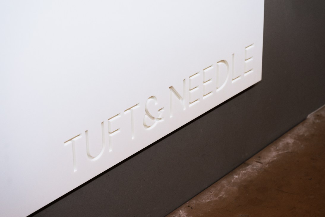 Close-up of Tuft & Needle white signage on a dark surface with angled perspective.