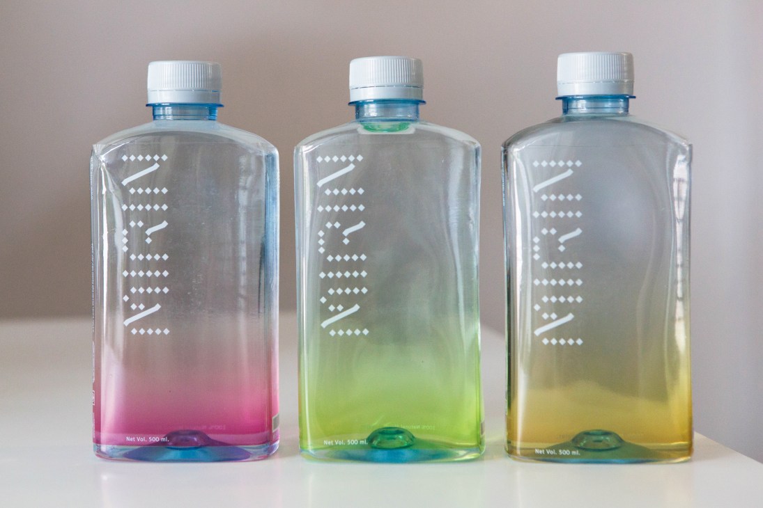 Three clear bottles with gradient colored liquids in pink, green, and yellow with geometric white dot patterns