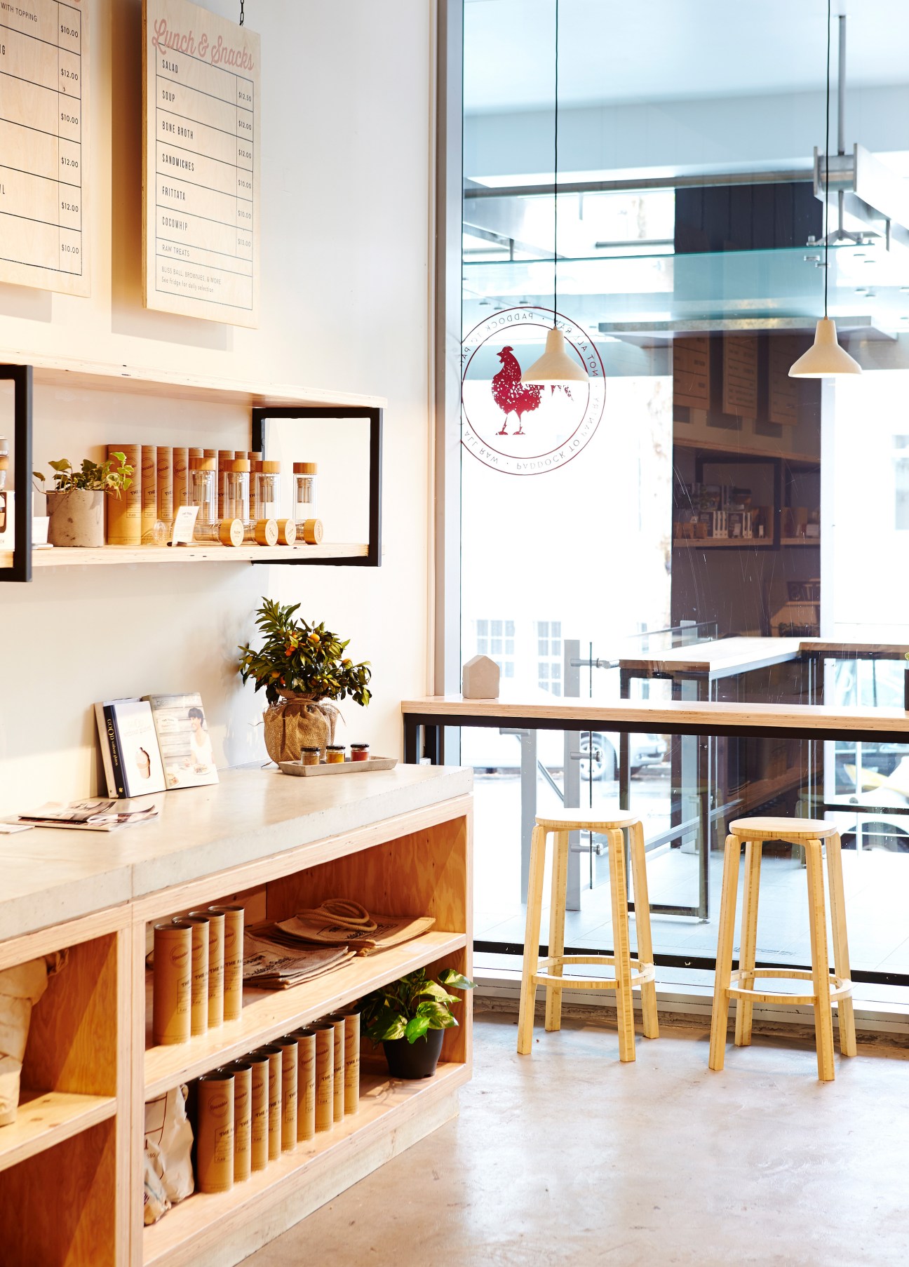 Interior of The Farm Wholefoods café with wooden shelving, menu board, pendant lighting and counter seating overlooking Sydney.