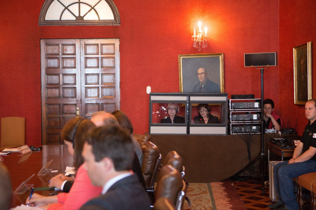 Translators and officials in a red-walled room at the Colombian foreign ministry with video conferencing equipment.