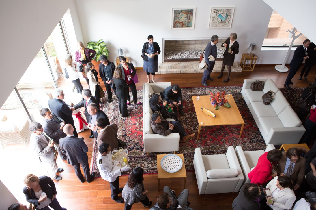 Aerial view of guests mingling at a modern residence with wooden floors, white furniture, and natural lighting from large windows.