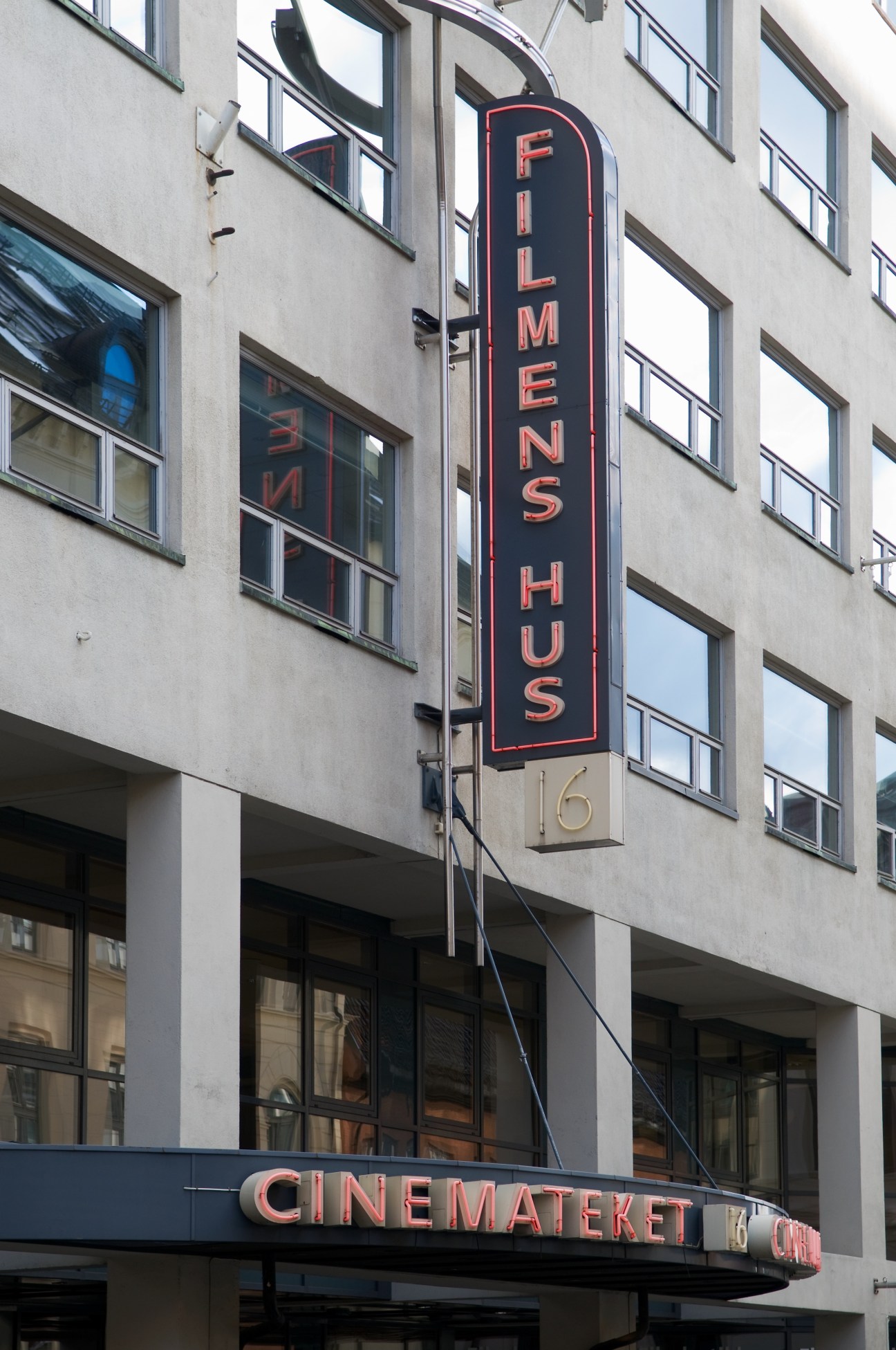 Red neon sign reading "FILMENS HUS" mounted on a modernist building facade.