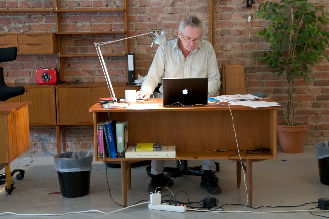 Peter Bøe, a consultant for Medieoperatørene, works at a wooden desk with a laptop in a brick-walled office.