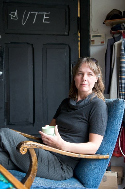 KriStine Ann Skaret, a producer at Medieoperatørene, sits holding a cup in an office with a blackboard marked "UTE" behind her.