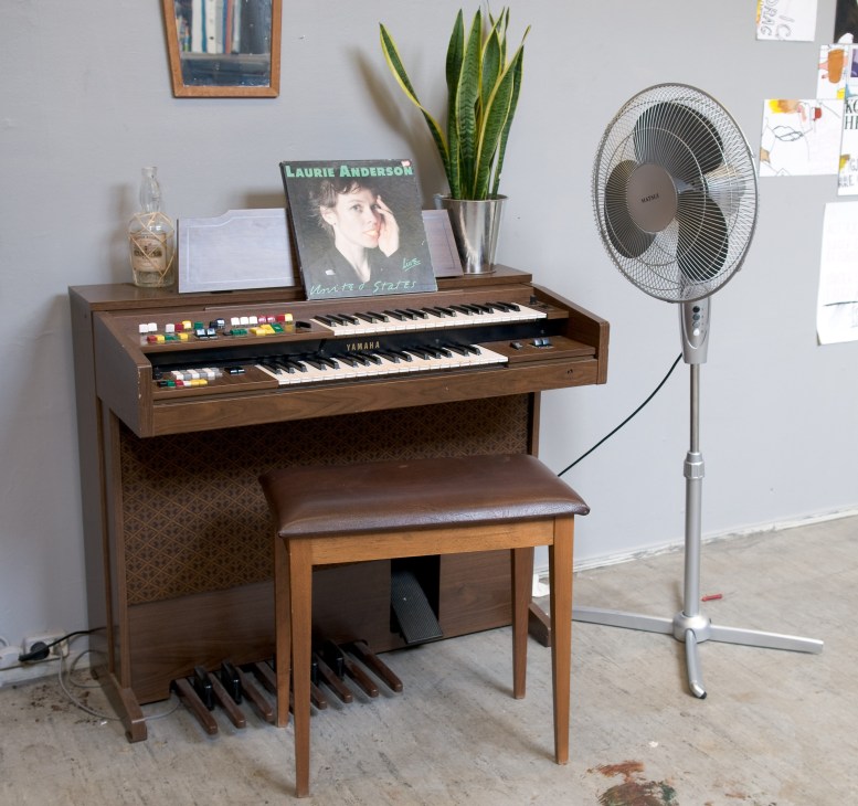Yamaha organ with dual keyboards next to a standing fan in a creative workspace.