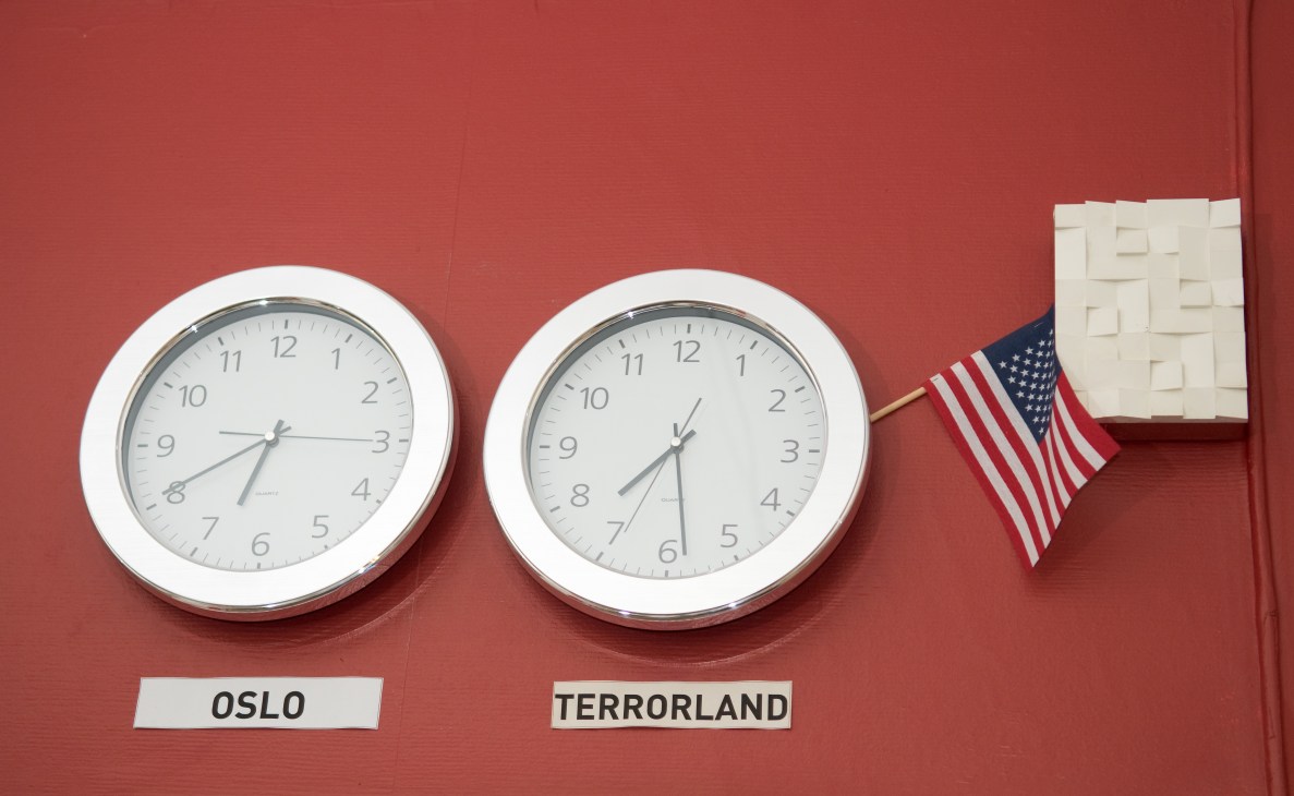 Two clocks on a red wall labeled Oslo and Terrorland with a small American flag between them.