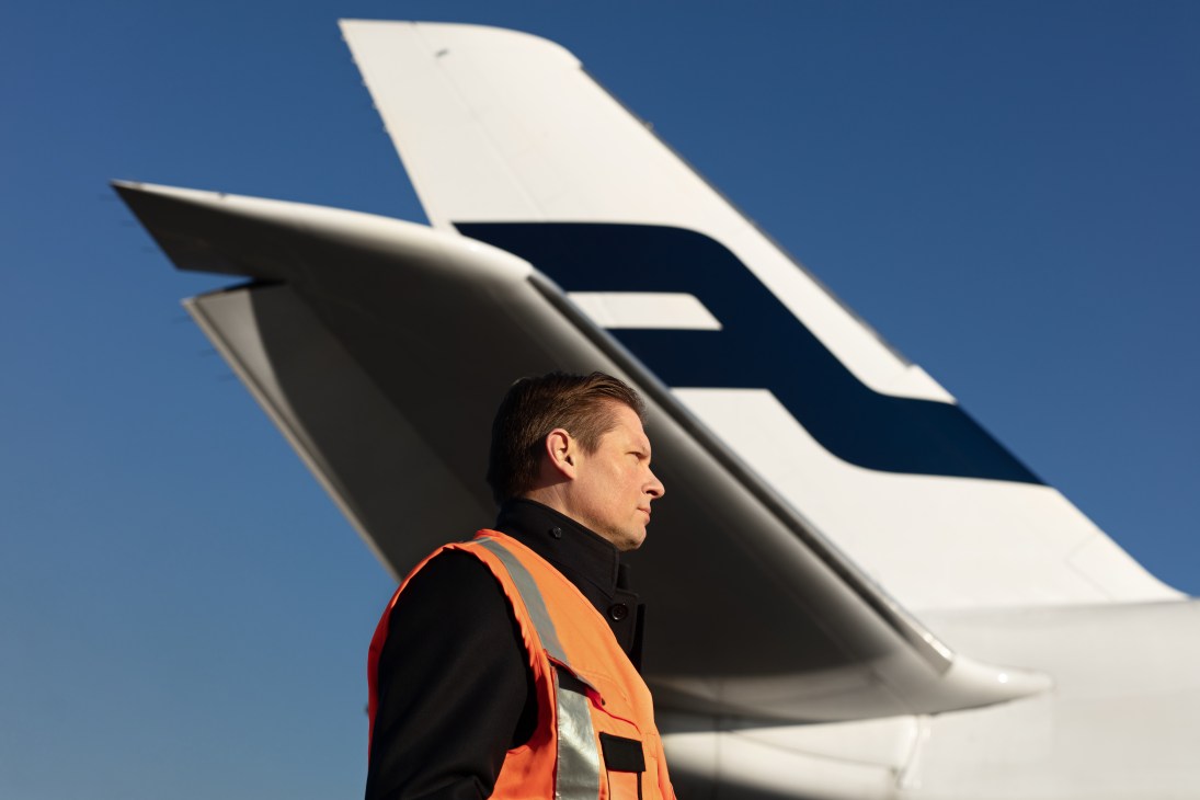 Finnair CEO Topi Manner in orange safety vest standing before aircraft tail fin.