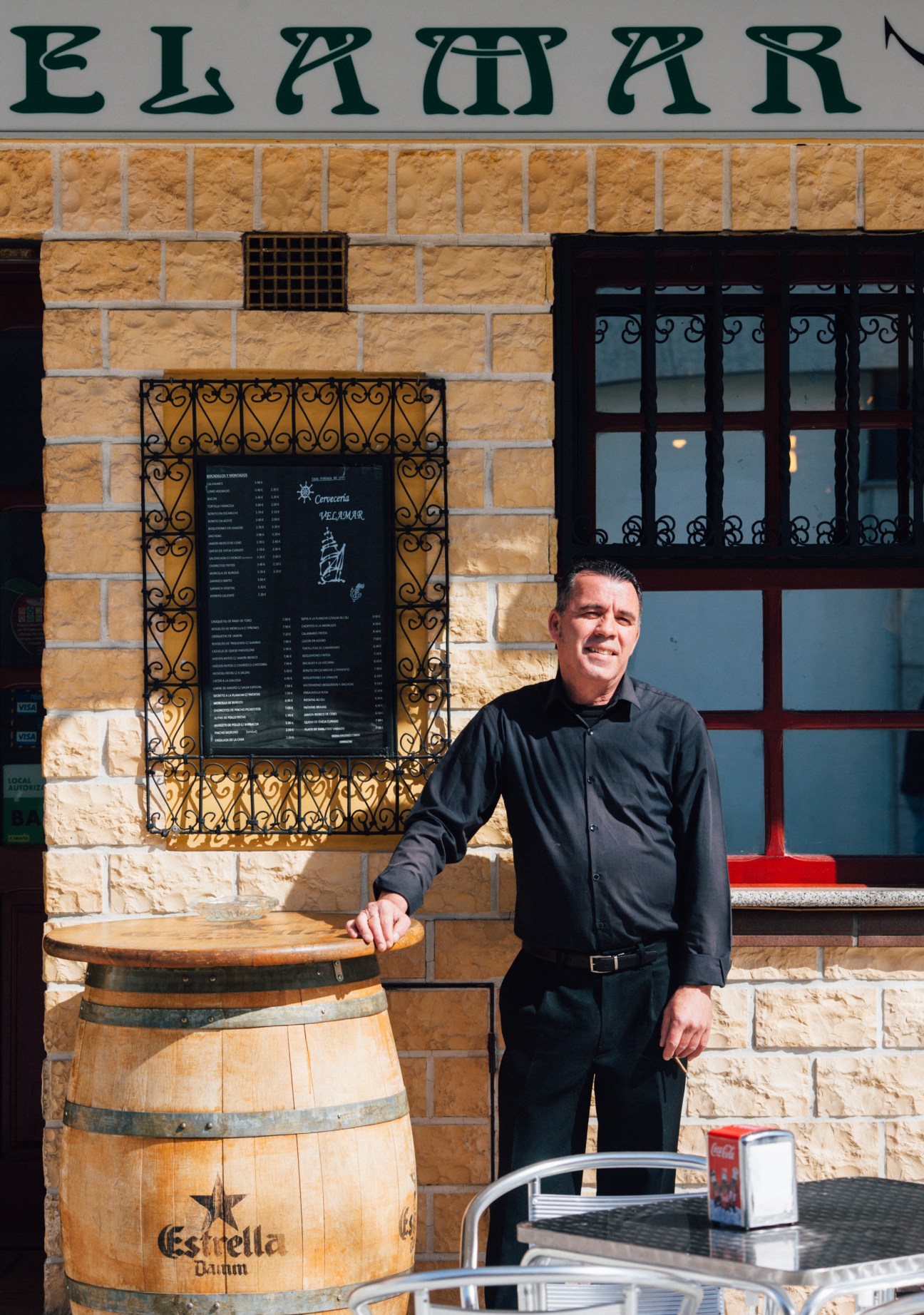 Man in black shirt stands outside a traditional bar storefront with stone facade and ornate ironwork.