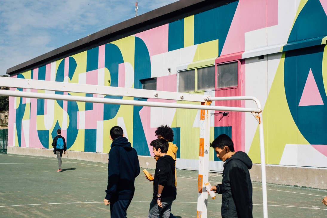 Students playing sports in front of a colorful geometric mural at a high school building in Torrelodones.