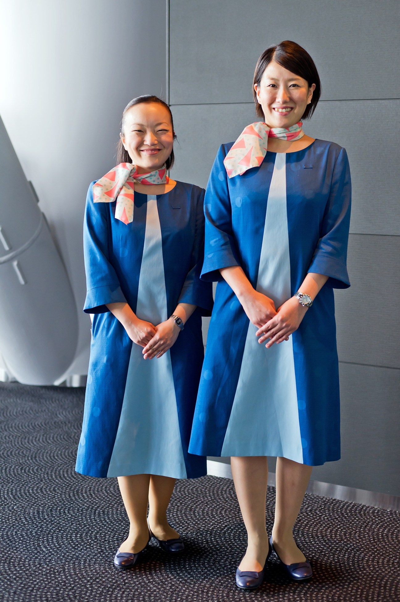 Two Tokyo Skytree ticket counter staff members wearing blue and light blue dresses with patterned scarves designed by Akira Minagawa.
