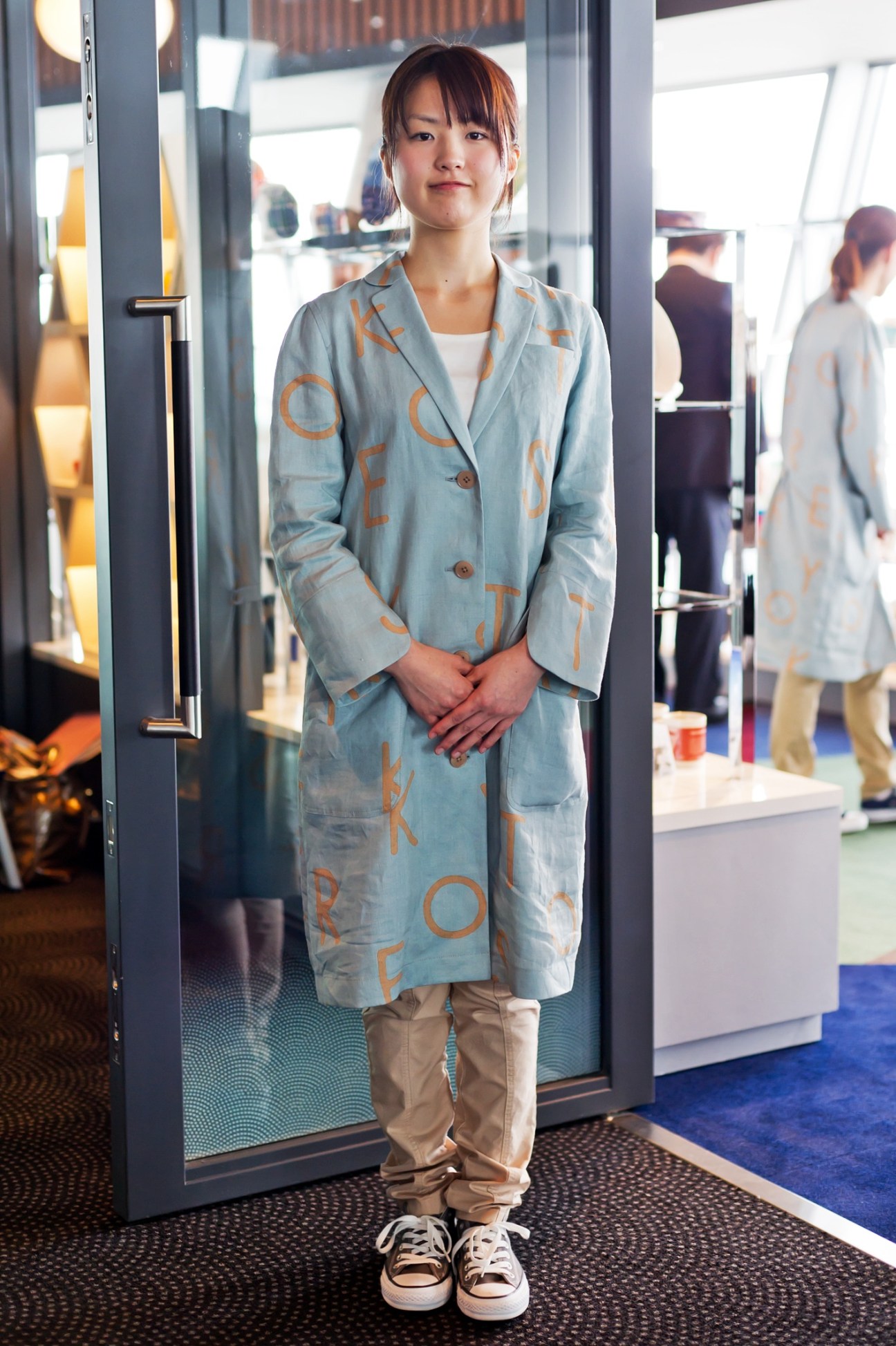 Tokyo Skytree shop staff member wearing a light blue linen overcoat designed by Akira Minagawa with orange tower motif pattern.