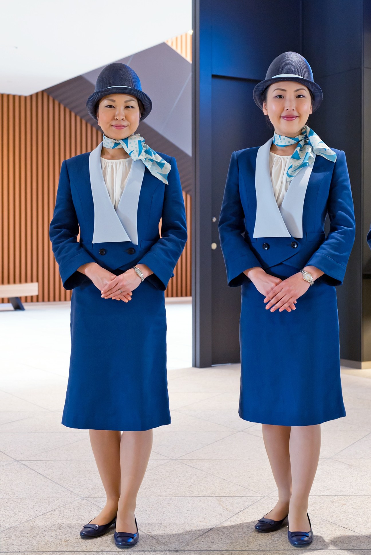 Two Tokyo Skytree information desk staff wearing blue uniforms with white vests and patterned scarves designed by Akira Minagawa.