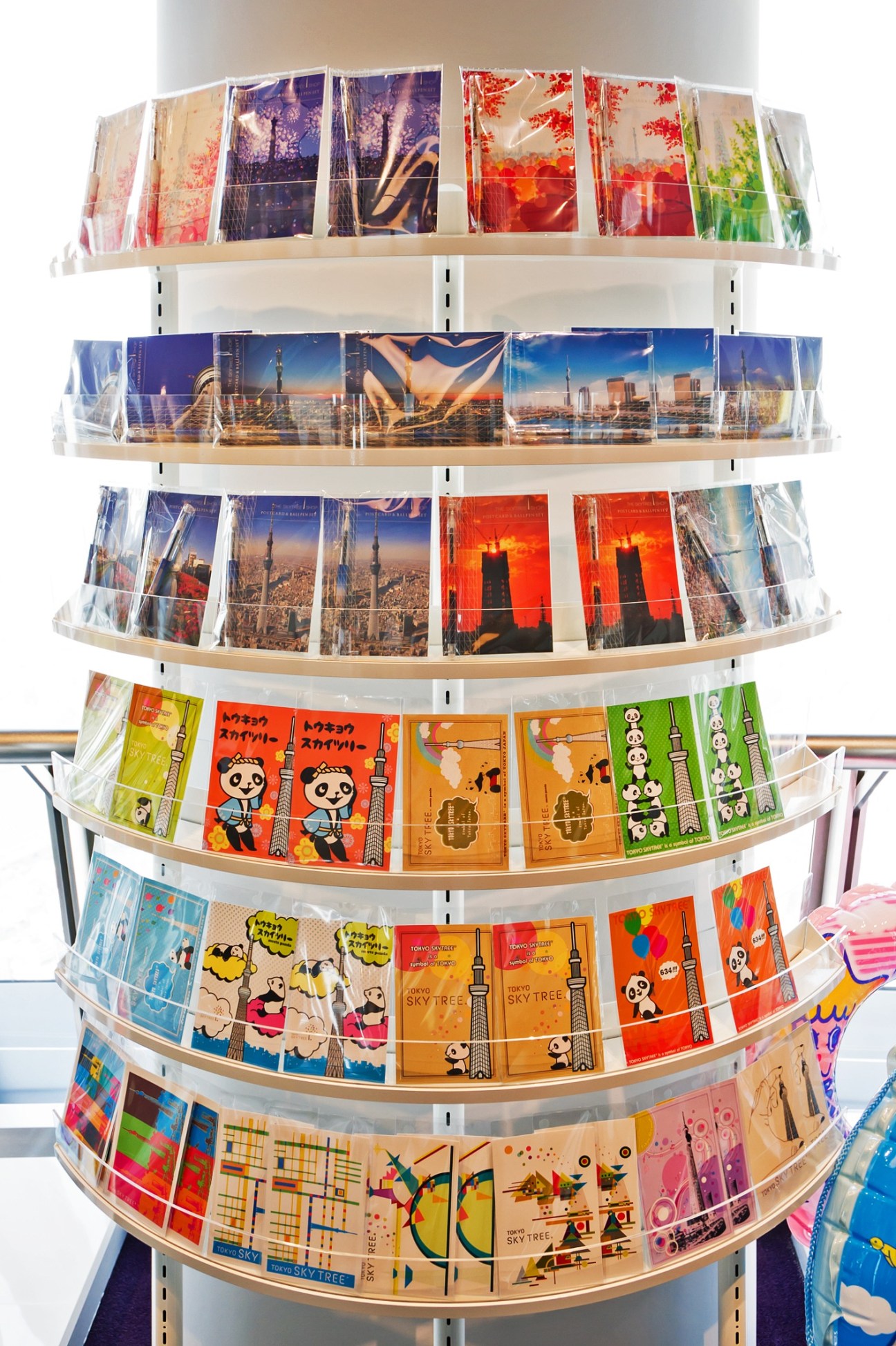 Curved display rack holding multiple shelves of colorful Tokyo Skytree postcards with various designs and imagery.