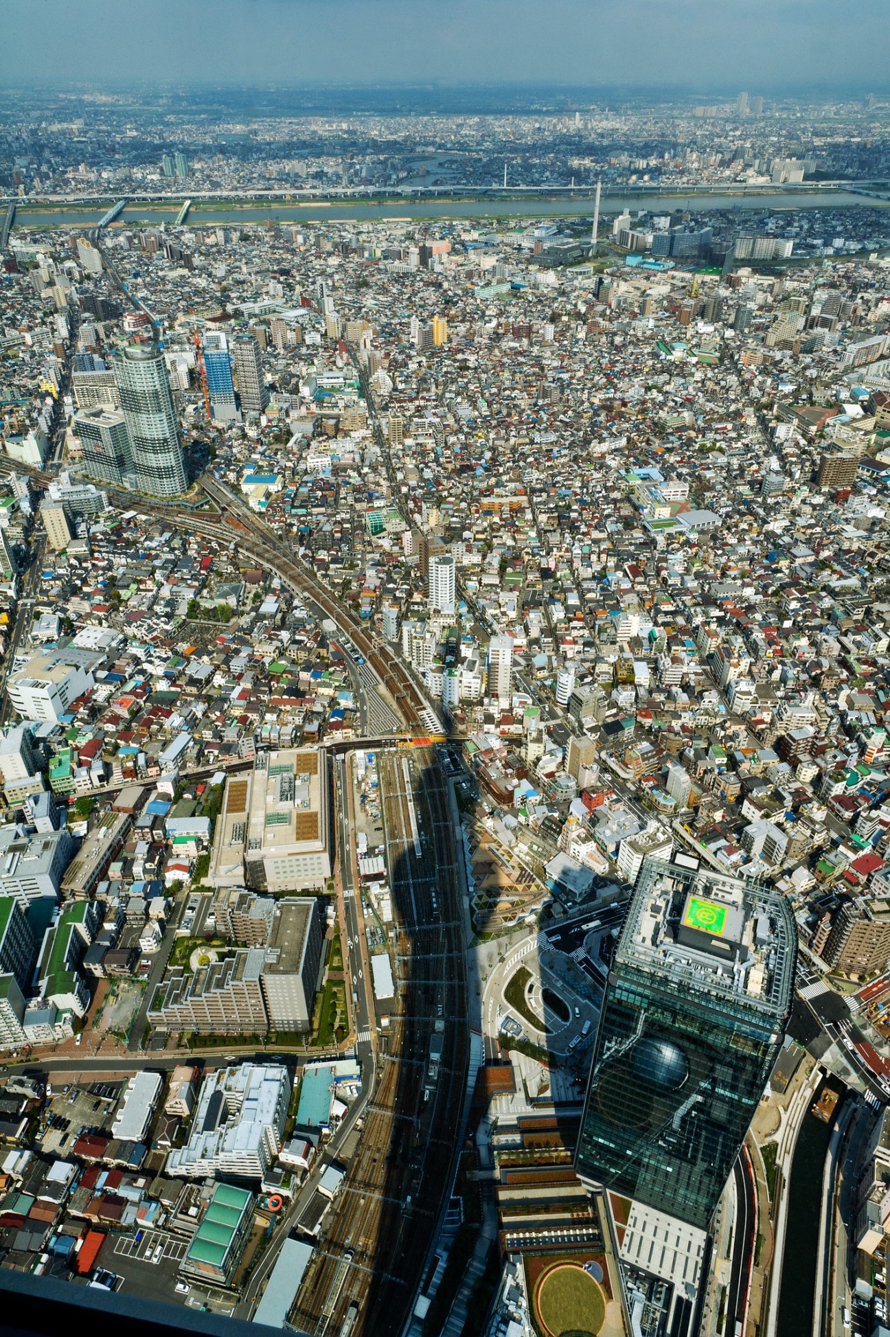 Aerial view of Tokyo cityscape taken from Tokyo Skytree observation deck, showing dense urban landscape with river and surrounding buildings.