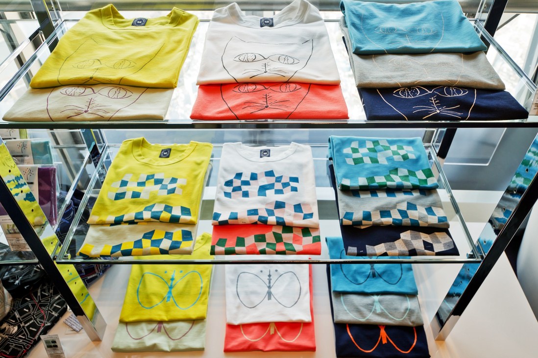 Minä Perhonen T-shirts designed by Akira Minagawa displayed on shelves in the Tokyo Skytree shop, featuring tower motifs and geometric patterns in various colors.