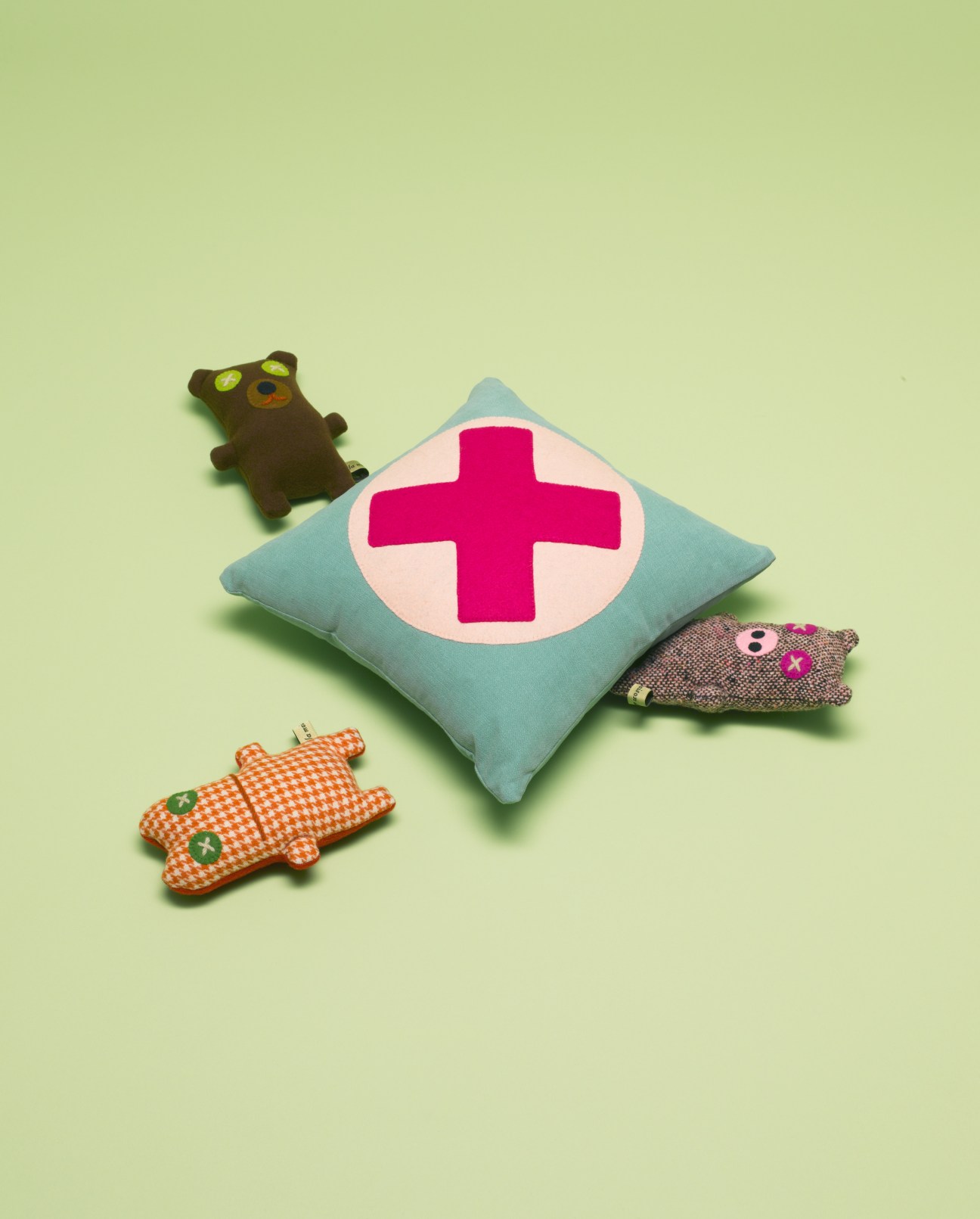 Hand-sewn wool dolls from La Maison de Lola displayed on a pale green background, including a blue pillow with a pink cross and animal-shaped toys.
