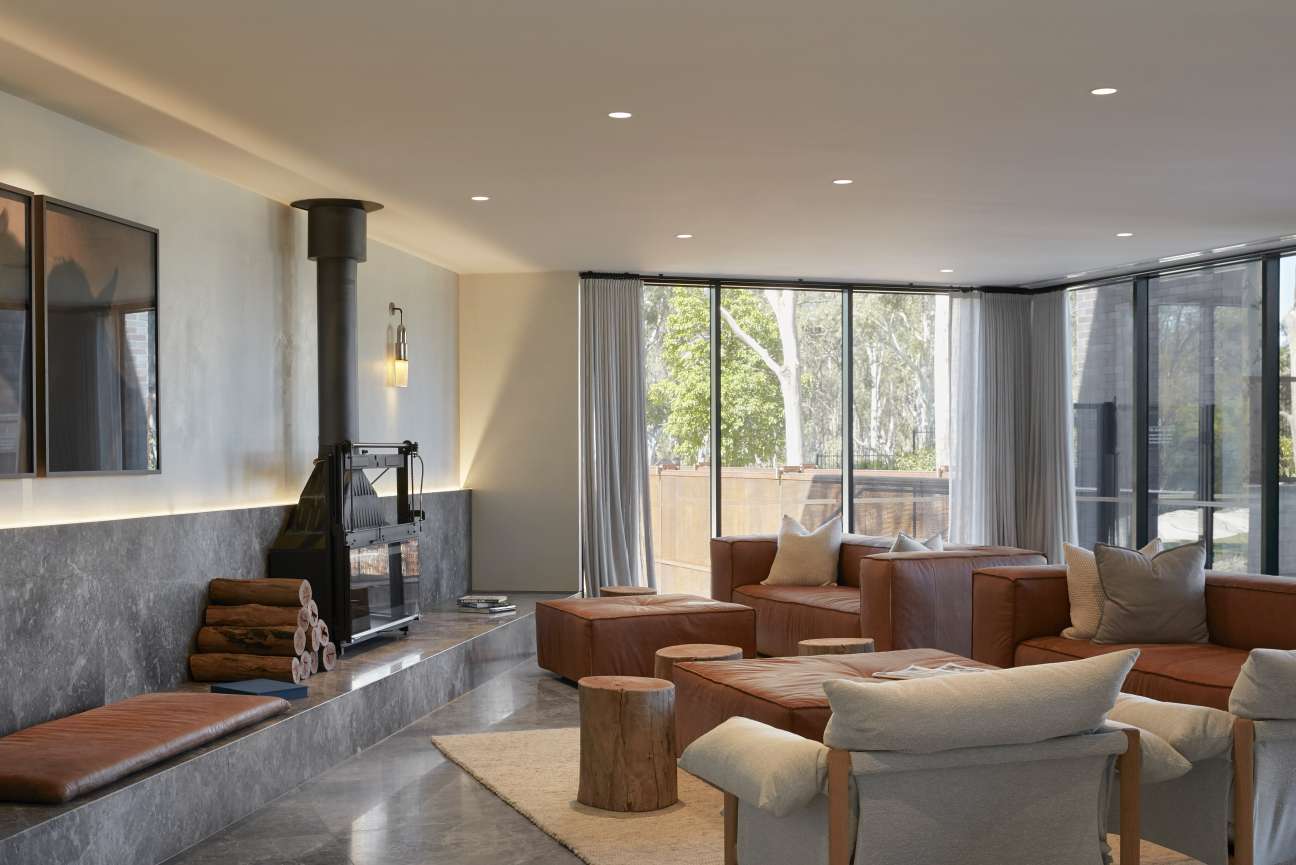 Modern hotel lobby with leather seating, fireplace, and large windows overlooking gum trees.