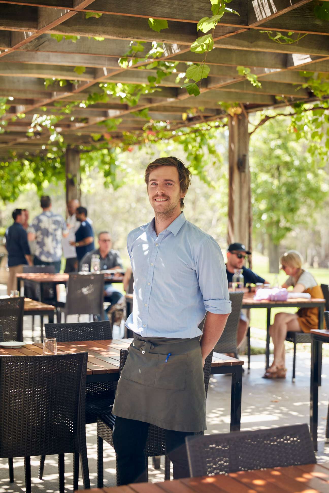 Restaurant employee at Muse standing in a pergola dining area with grapevines overhead.