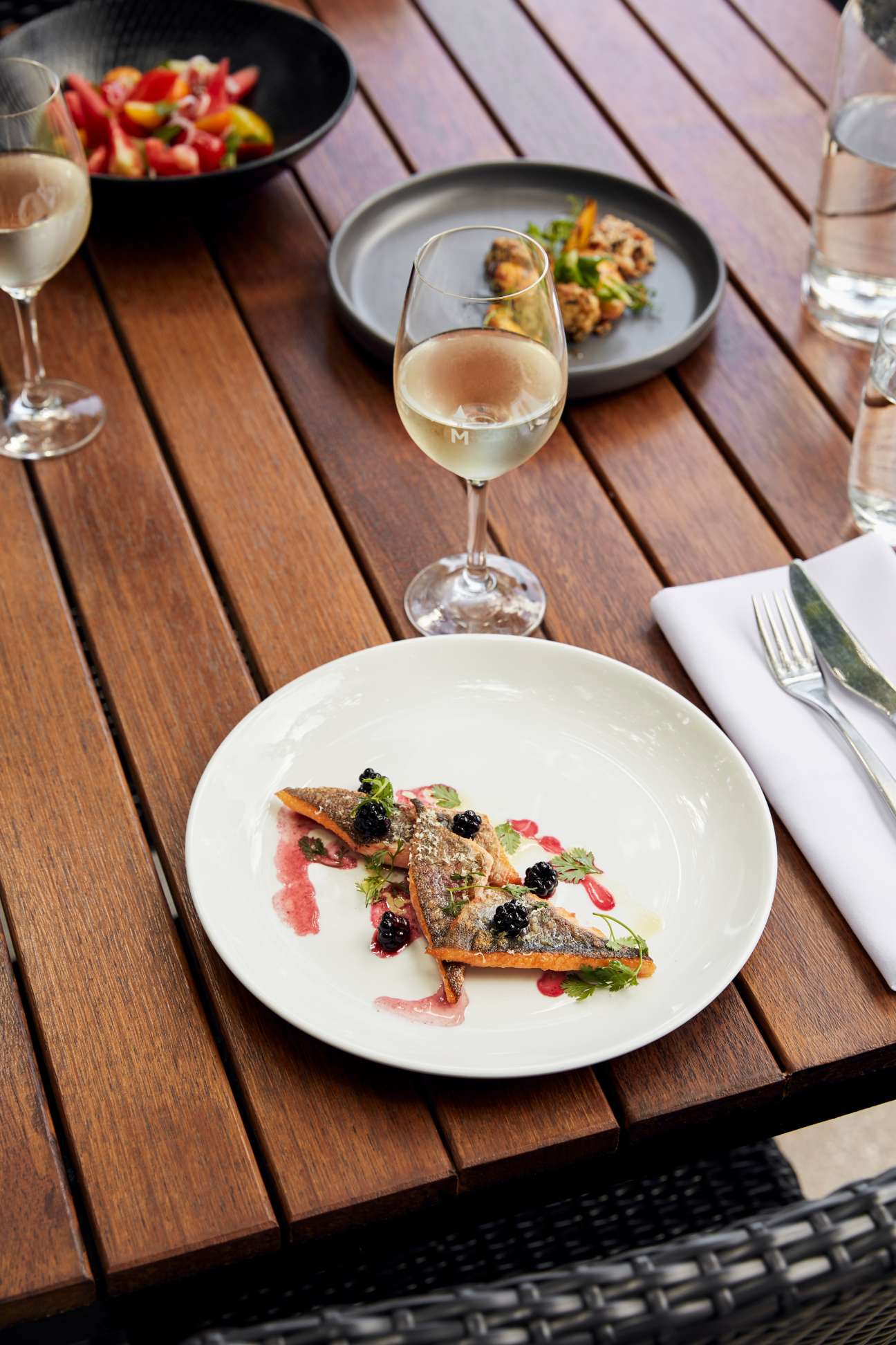 River trout with blackberries plated on white dish with wine pairing on wooden table.