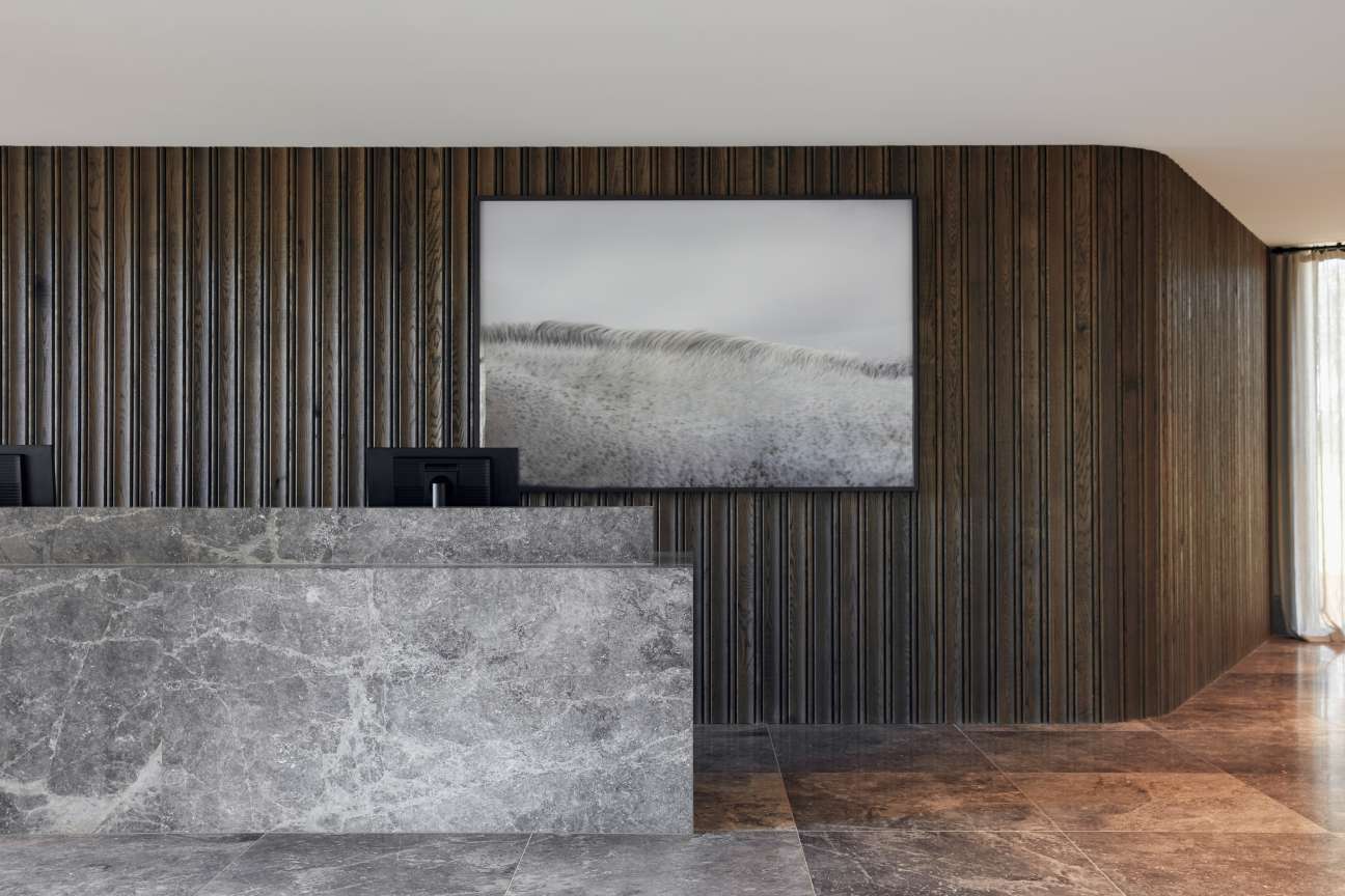 Modern hotel lobby with vertical wood paneling, marble counter, and framed landscape photograph on wall.