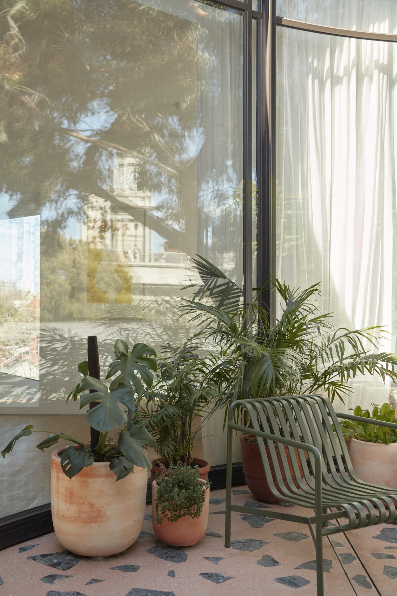Apartment terrace with potted plants, modern chair, and views of eucalyptus trees through large windows.