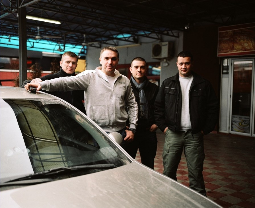 Four armed bodyguards stand beside an unmarked car outside a building, providing security for investigative journalist Brankica Stankovic.