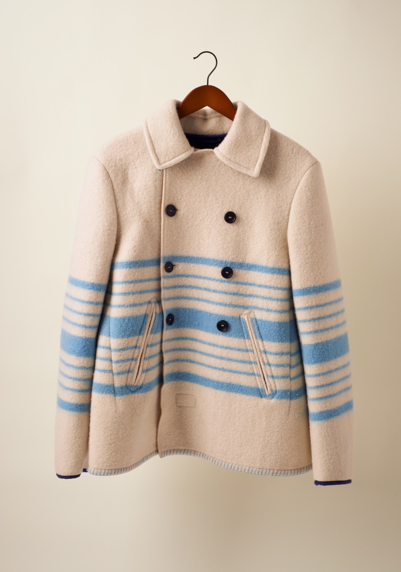 Cream and blue striped wool jacket with double-breasted buttons on wooden hanger.