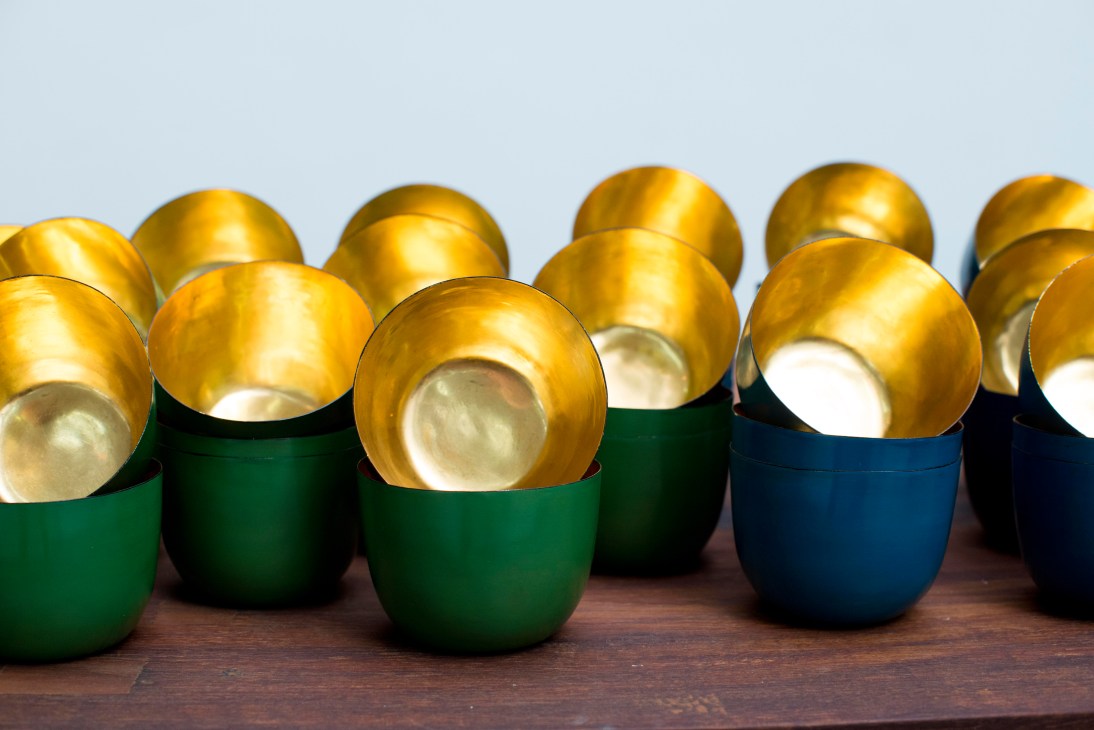 Handcrafted lacquer bowls with gold interiors and green and blue exterior finishes displayed on wood.