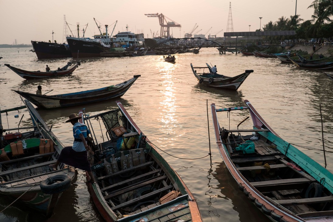 Yangon riverfront with traditional wooden boats and shipping vessels at sunset.