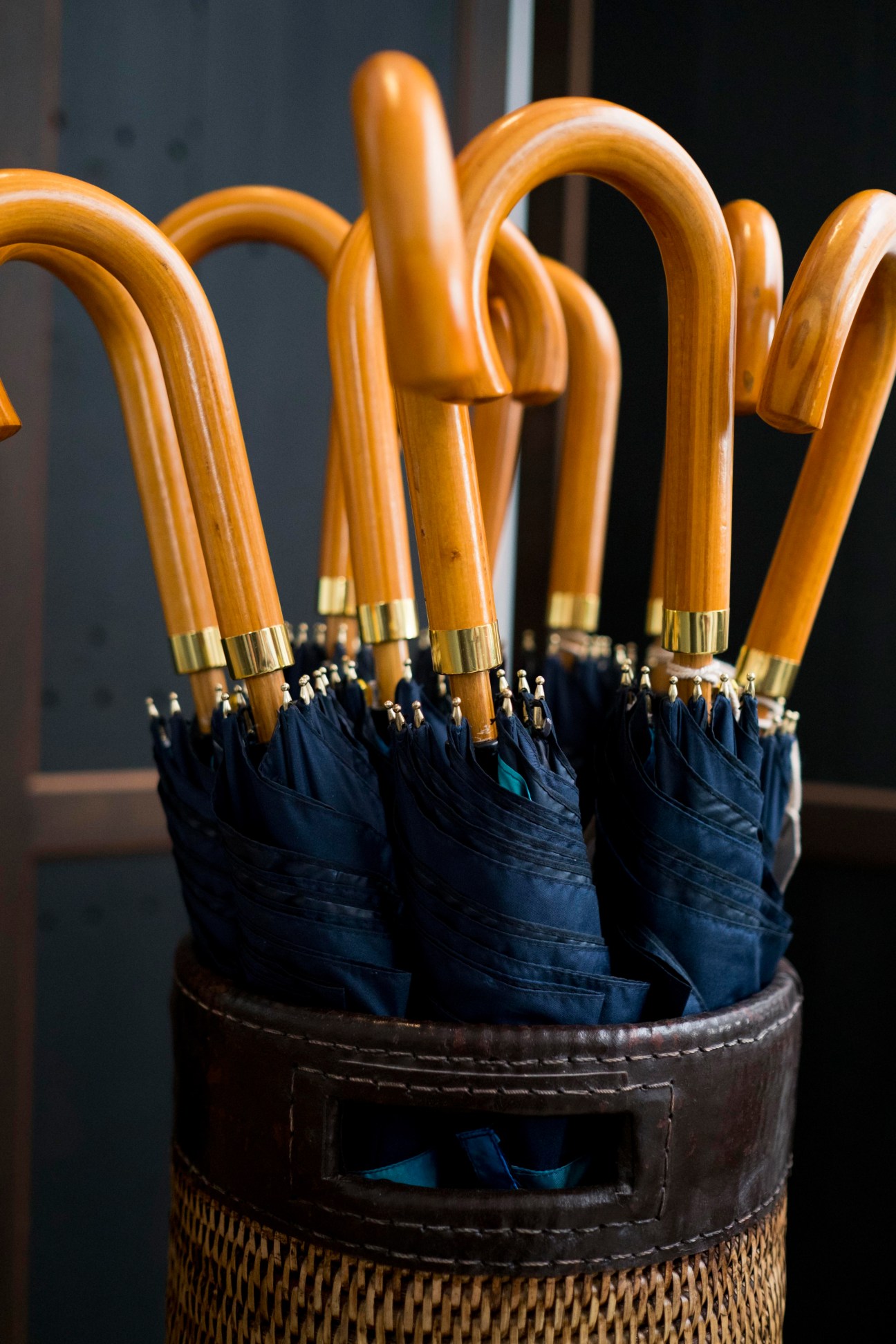 Handmade umbrellas with wooden curved handles and dark blue fabric displayed in a woven basket.