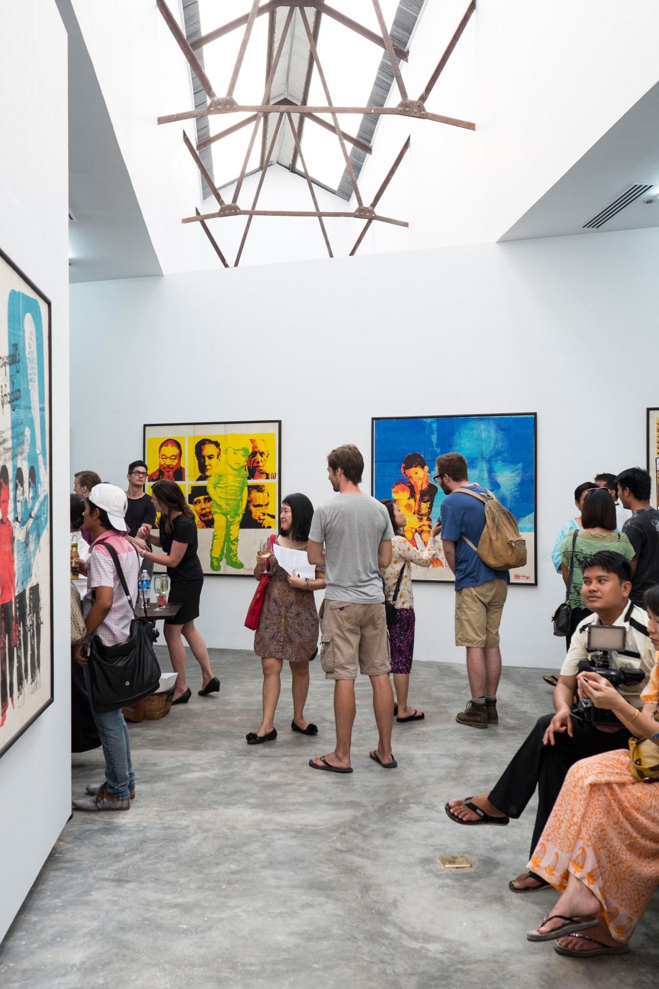 Visitors view colorful contemporary art exhibitions in TS1's minimalist white gallery space with geometric ceiling fixture.