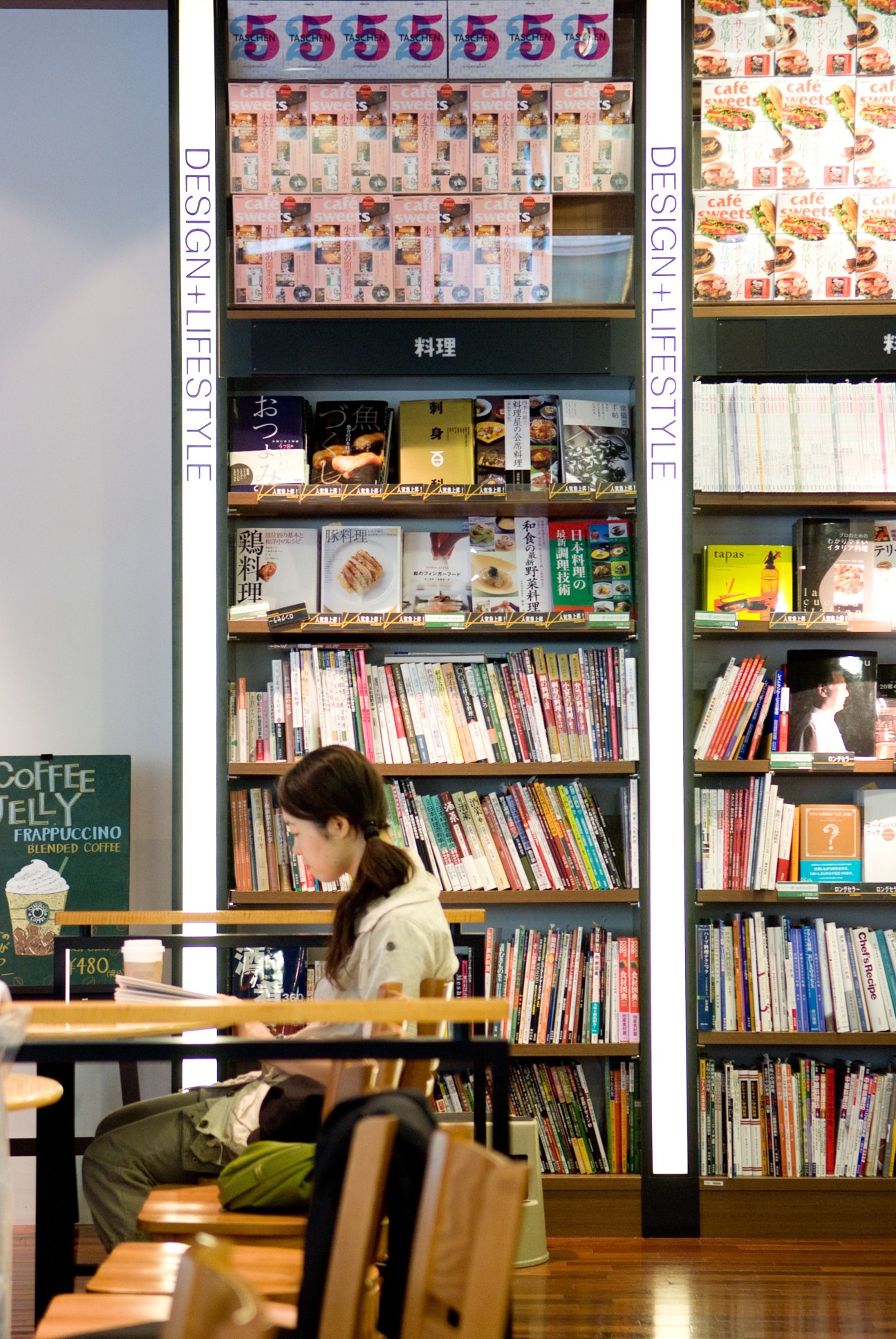 Customer browsing books in a modern café with shelves displaying design and food magazines in Japanese.