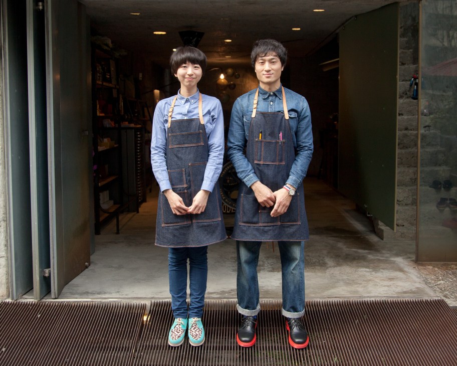 Two people wearing denim aprons standing in the entrance of Tools to Live By shop.