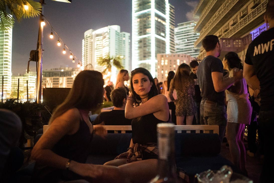 People gathered on a rooftop terrace at night with illuminated high-rise buildings in the background.
