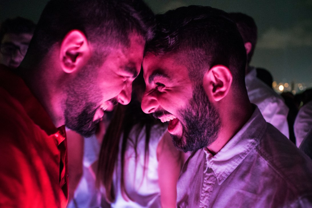 Two men laughing together under pink and purple nightclub lighting.
