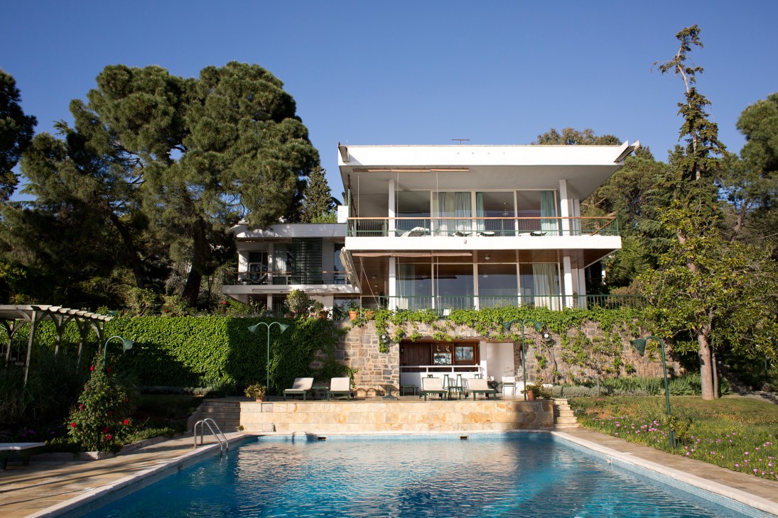 Mid-century modern white concrete house with multiple terraces overlooking a swimming pool and surrounding gardens on Buyukada island.
