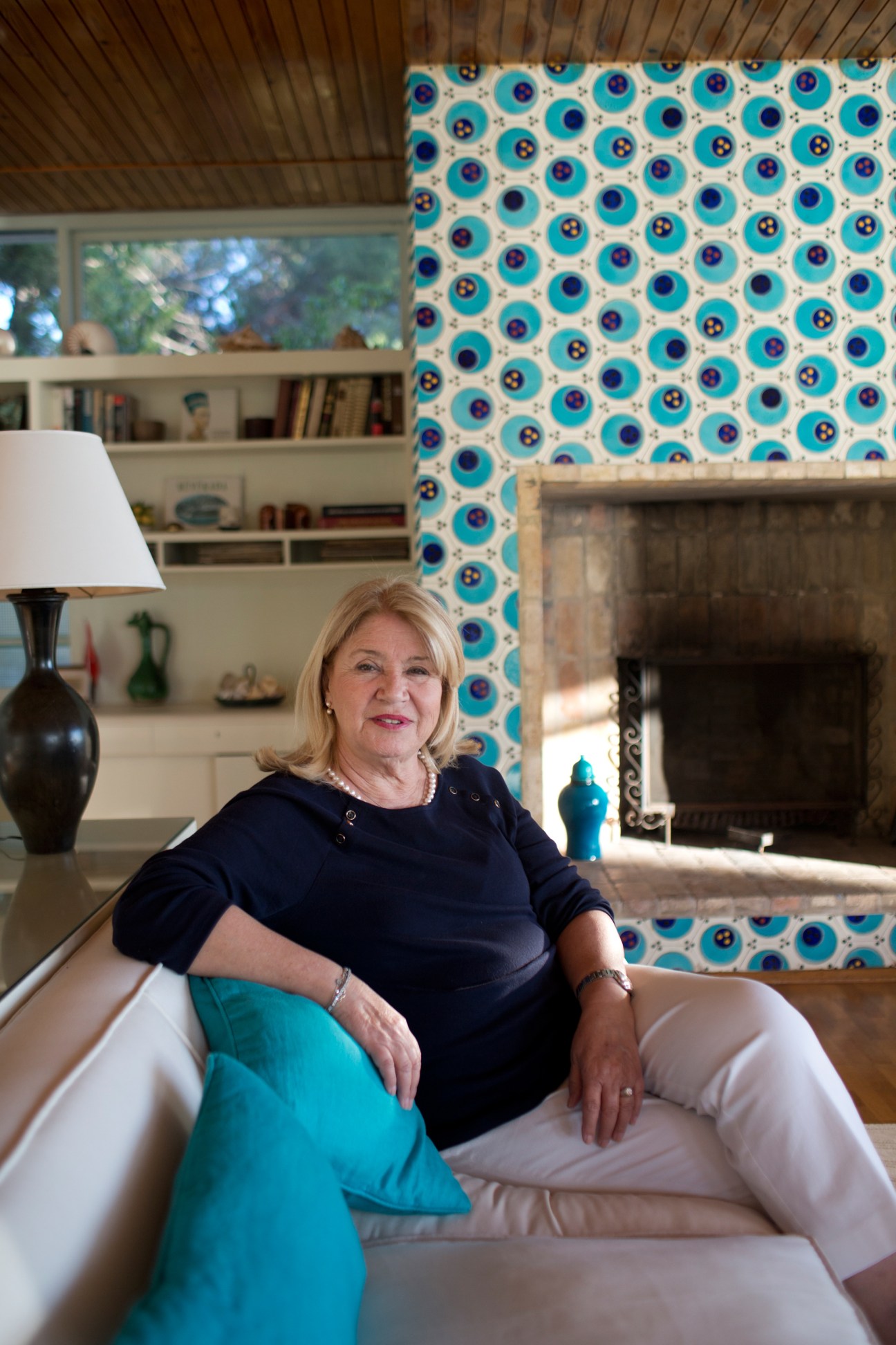Julide Neslihan Taki sits in the living room with turquoise tiled fireplace behind her.