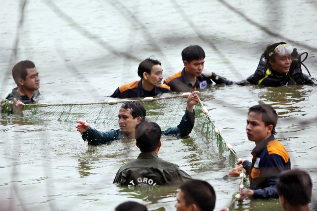 Multiple people in wetsuits stand in murky water holding a large fishing net.
