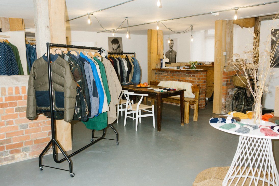 The Workers Club showroom interior with clothing displayed on racks, wooden table, brick fireplace, and vintage bicycle.