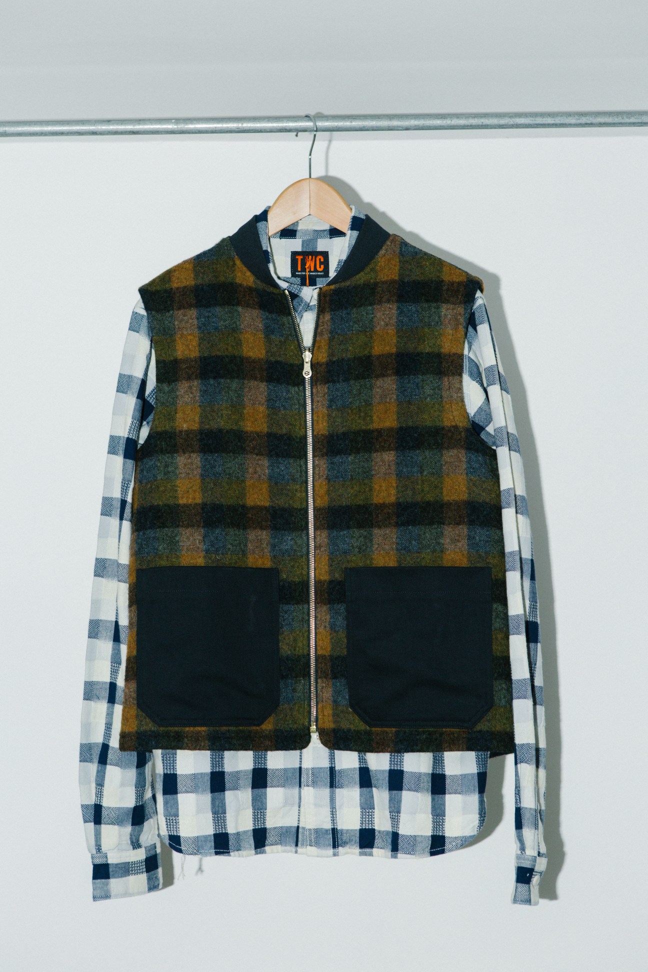 Checked-wool gilet in brown and teal plaid over blue and white checkered shirt on wooden hanger