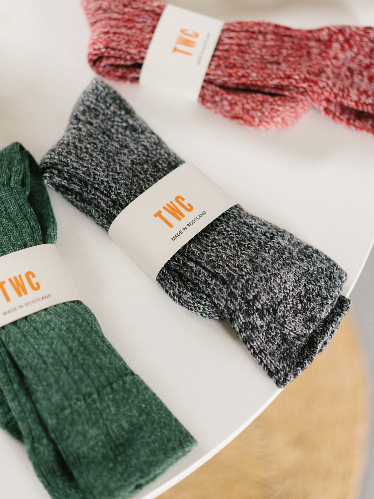 The Workers Club merino-wool socks in red, grey and green with white branded labels on white surface.