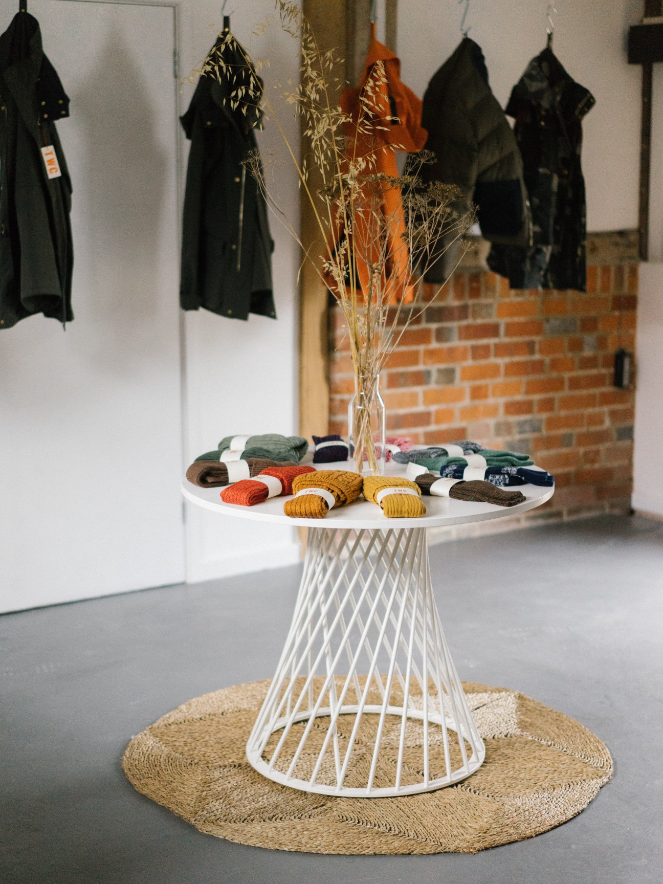 The Workers Club showroom displaying folded socks and jackets on a white pedestal table with dried flowers.
