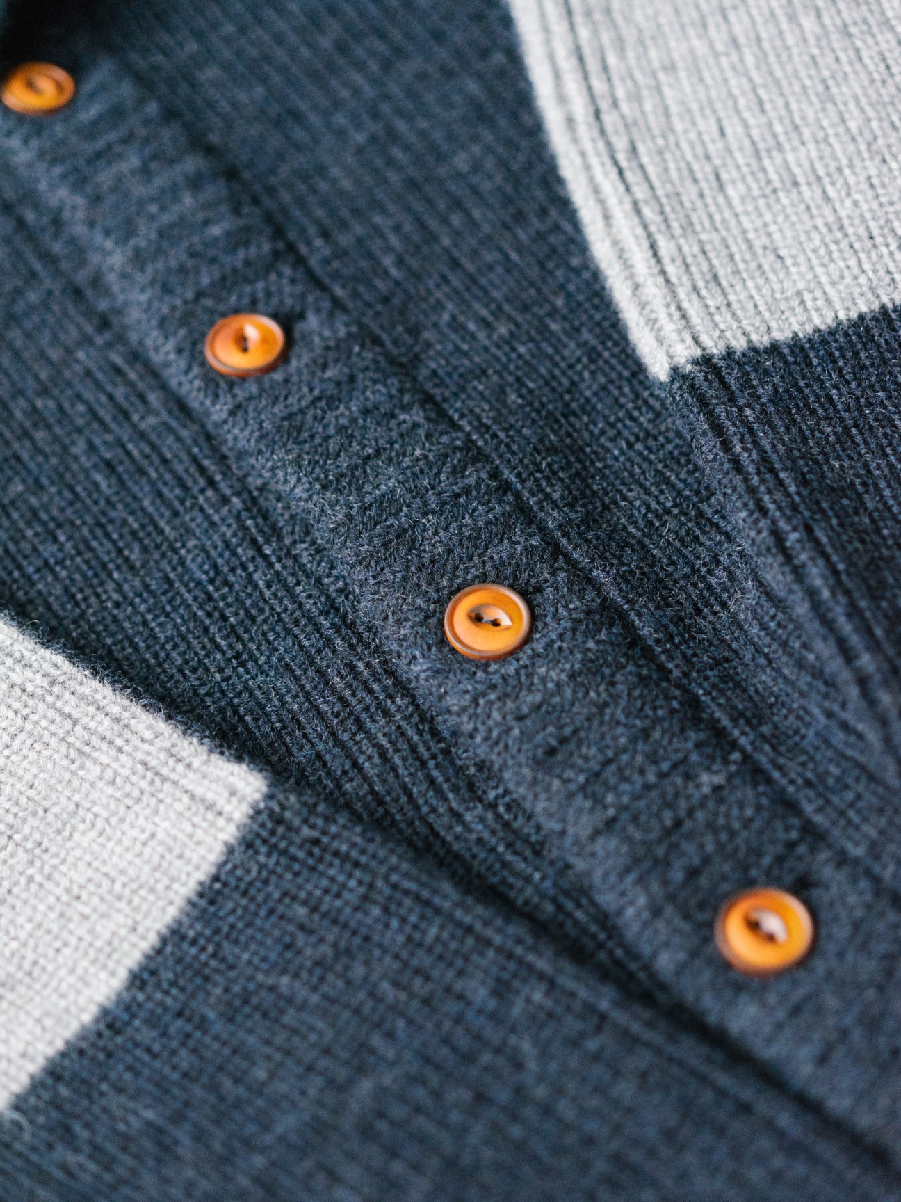 Dark navy knit cardigan with amber buttons displayed on white background.