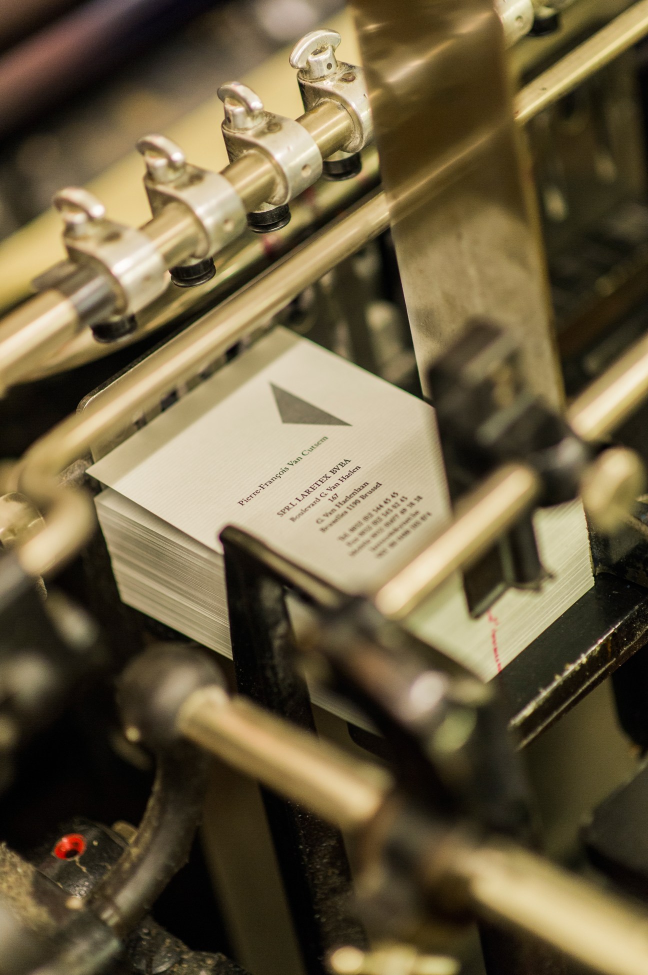 Business cards being printed on a Heidelberg press with brass clamps holding paper in place.