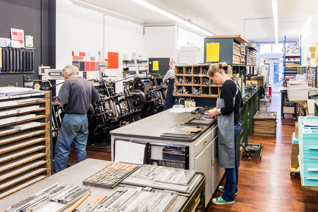 Workers in Le Typographe's Brussels workshop arrange lead type and operate Heidelberg printing presses.