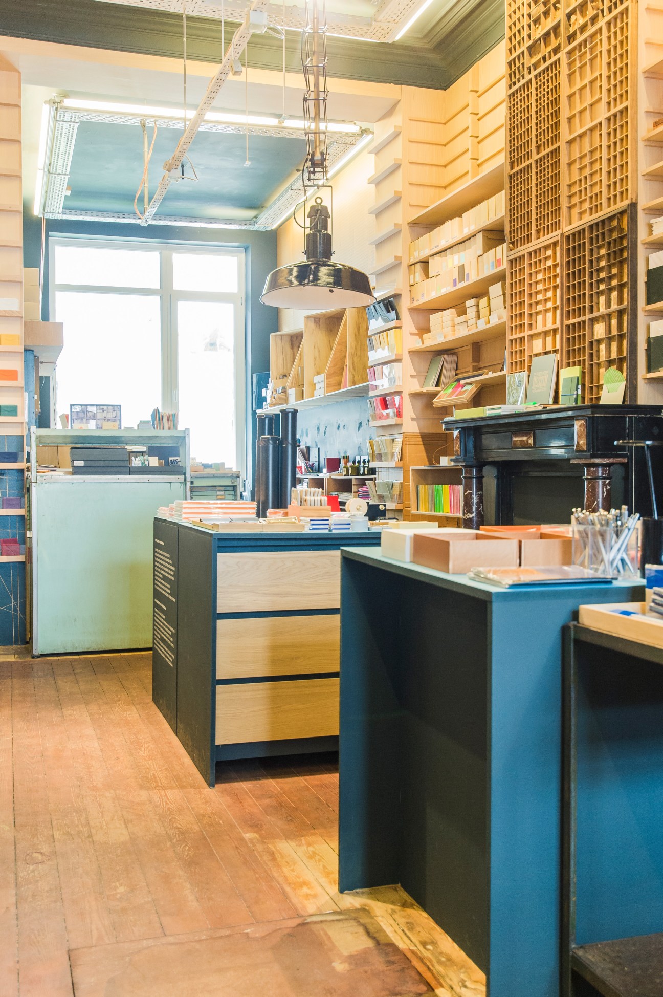 Le Typographe's retail shop interior with wooden shelving displaying stationery and books, blue-painted counters, and pendant lighting.