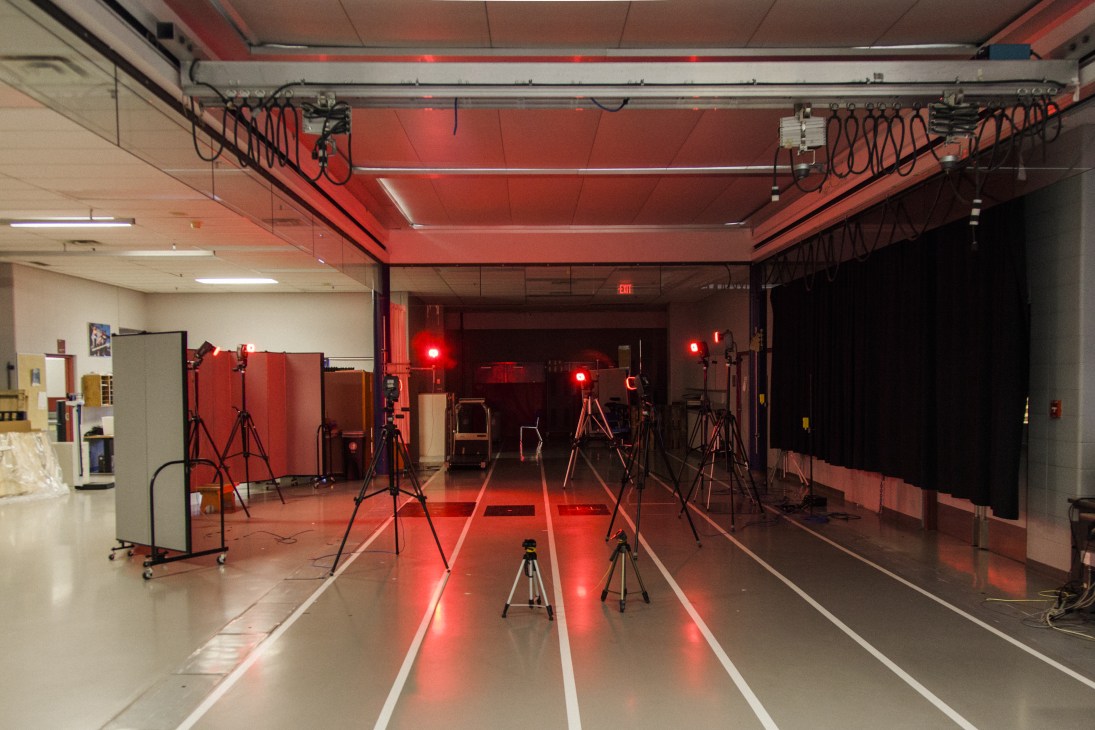 Red-lit biomechanics laboratory with multiple camera tripods and lighting equipment set up for motion capture testing.