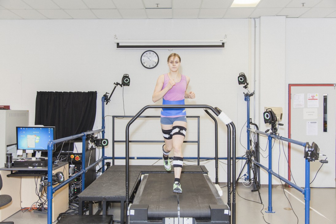 Runner on treadmill surrounded by motion-capture equipment and cameras in a biomechanics laboratory.