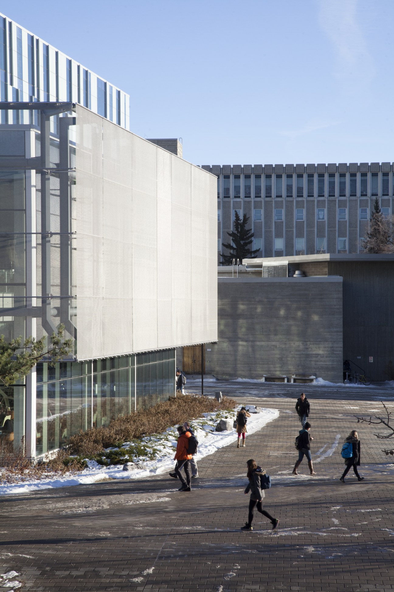 Modern campus courtyard with white and grey building facades, students walking on paved ground with patches of snow.